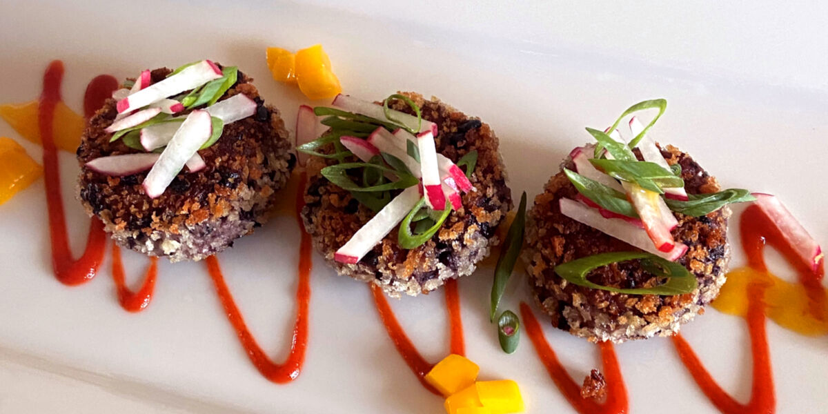 Three purple Copi Cakes topped with slivered radish, chopped chives, and diced mangos